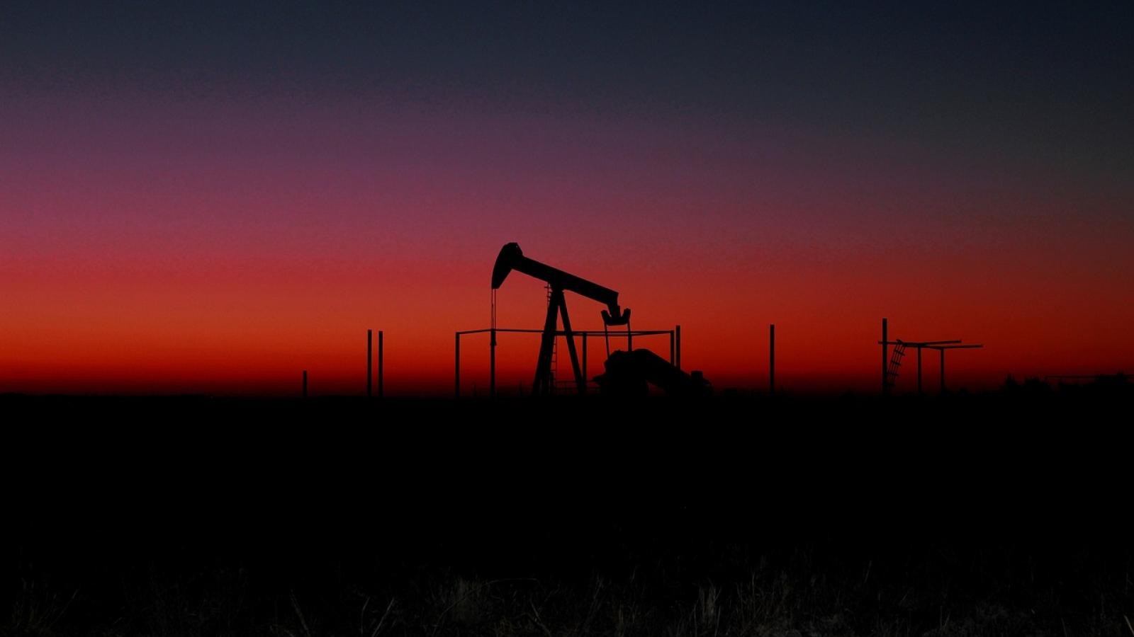 Pompe de pétrole au loin à la brunante sous un ciel coloré de rouge