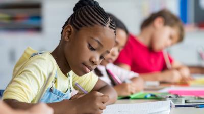 Jeune élève noire assise à son bureau en train d'écrire