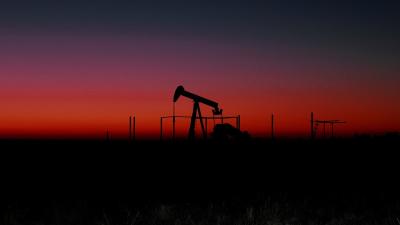 Pompe de pétrole au loin à la brunante sous un ciel coloré de rouge