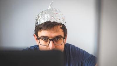Homme devant un ordinateur avec un chapeau en papier d'aluminium pour se protéger des ondes.