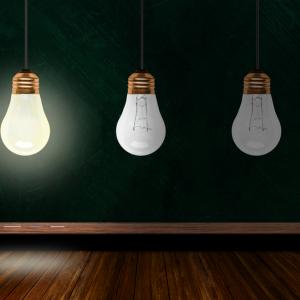 Une ampoule allumée et deux ampoules éteintes devant un tableau d'école pour imager le concept de créativité 