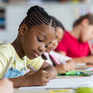 Jeune élève noire assise à son bureau en train d'écrire