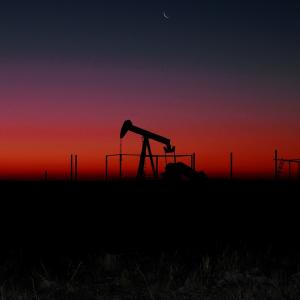 Pompe de pétrole au loin à la brunante sous un ciel coloré de rouge
