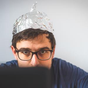 Homme devant un ordinateur avec un chapeau en papier d'aluminium pour se protéger des ondes.